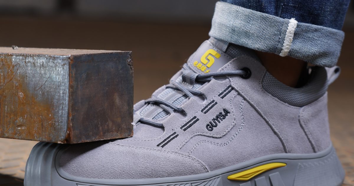 Grey suede safety sneaker next to a steel block, showing the protective toe area